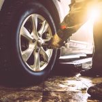 Mechanic hands with wrench changes wheel on car with special equipment in car repair service shop, sunlight effect, toned